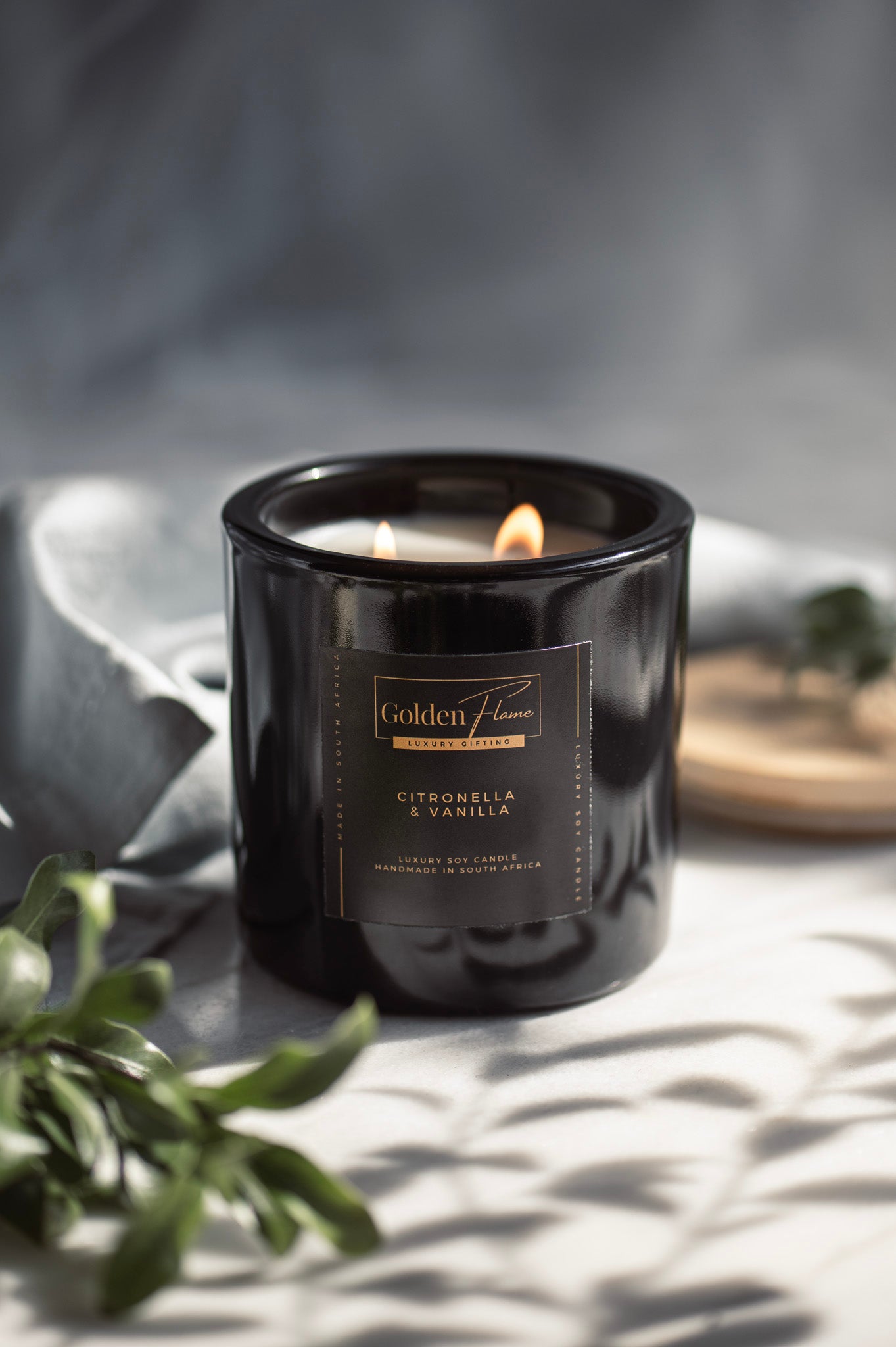 Black candle with a label on a light surface with greenery