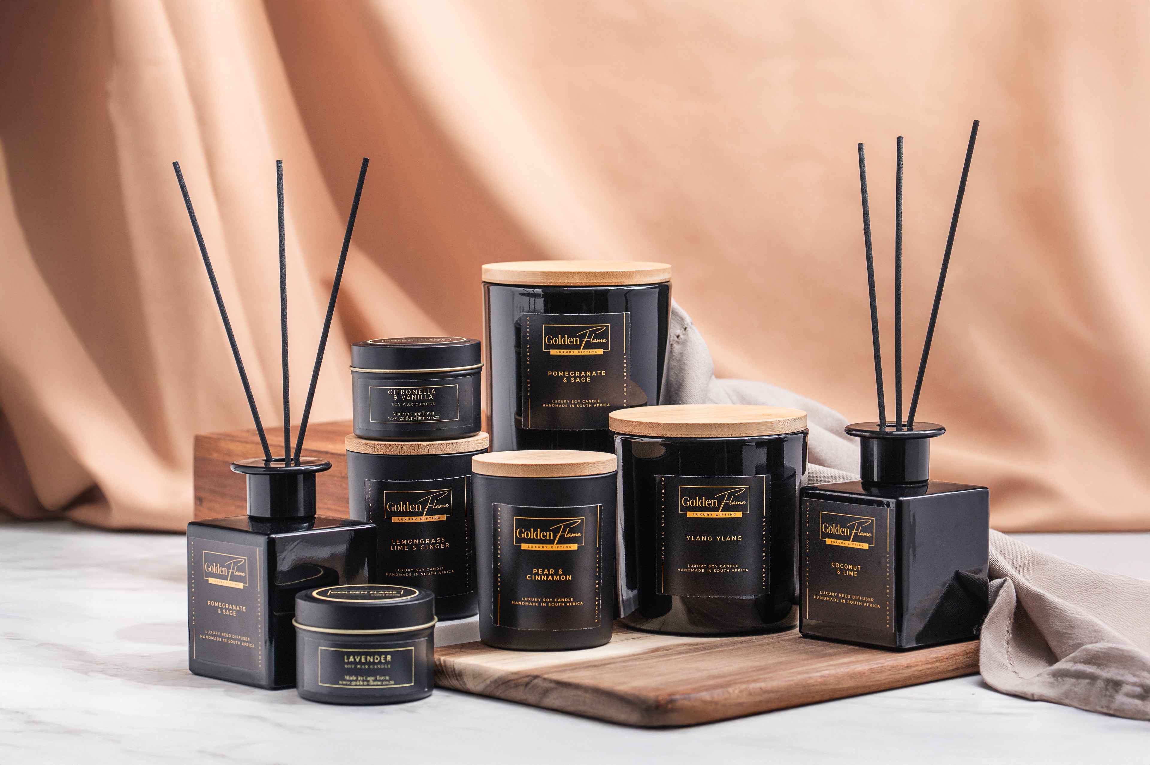 Collection of black and gold candles and diffusers on a neutral background