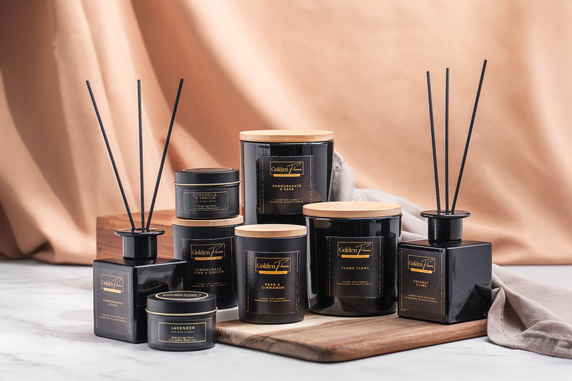 Collection of black and gold candles and diffusers on a neutral background